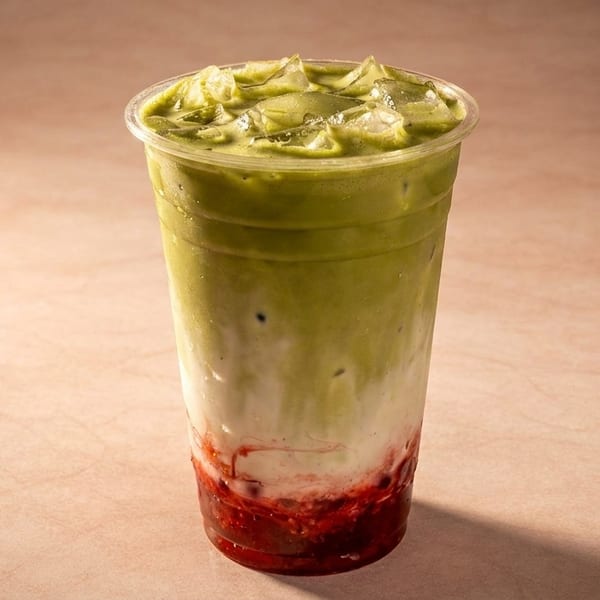 Iced matcha latte with strawberry puree and milk in a clear plastic cup.